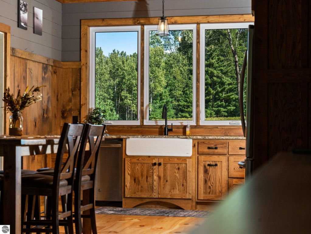 Open-concept kitchen with wooden cabinets, farmhouse sink, and large windows showcasing serene views of northern Michigan greenery.