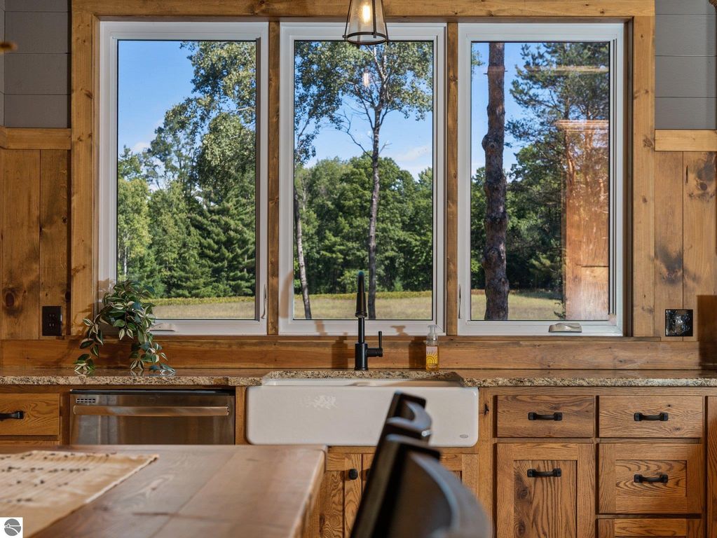 Kitchen interior with large windows showcasing serene northern Michigan countryside views, custom cabinetry, granite countertops, and farmhouse sink, highlighting the craftsmanship of the home at 5800 W Moorestown Road, Lake City, MI.