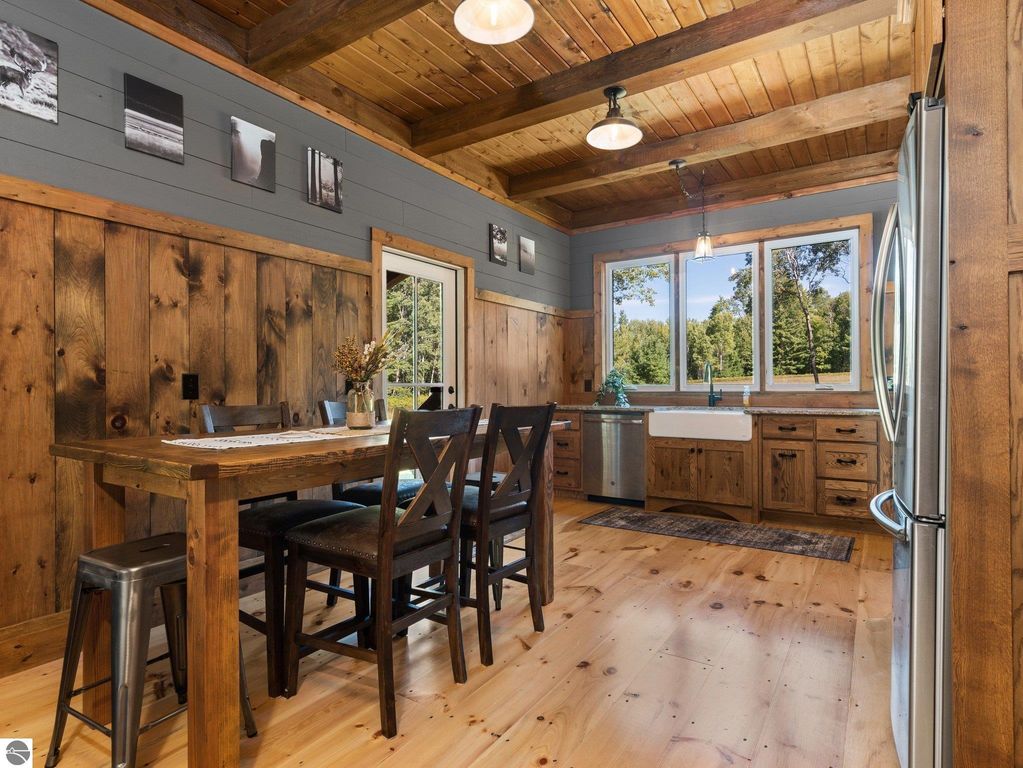 Custom-built kitchen featuring rustic wood finishes, large windows with scenic views, a farmhouse sink, and a dining table, highlighting craftsmanship in a northern Michigan home.