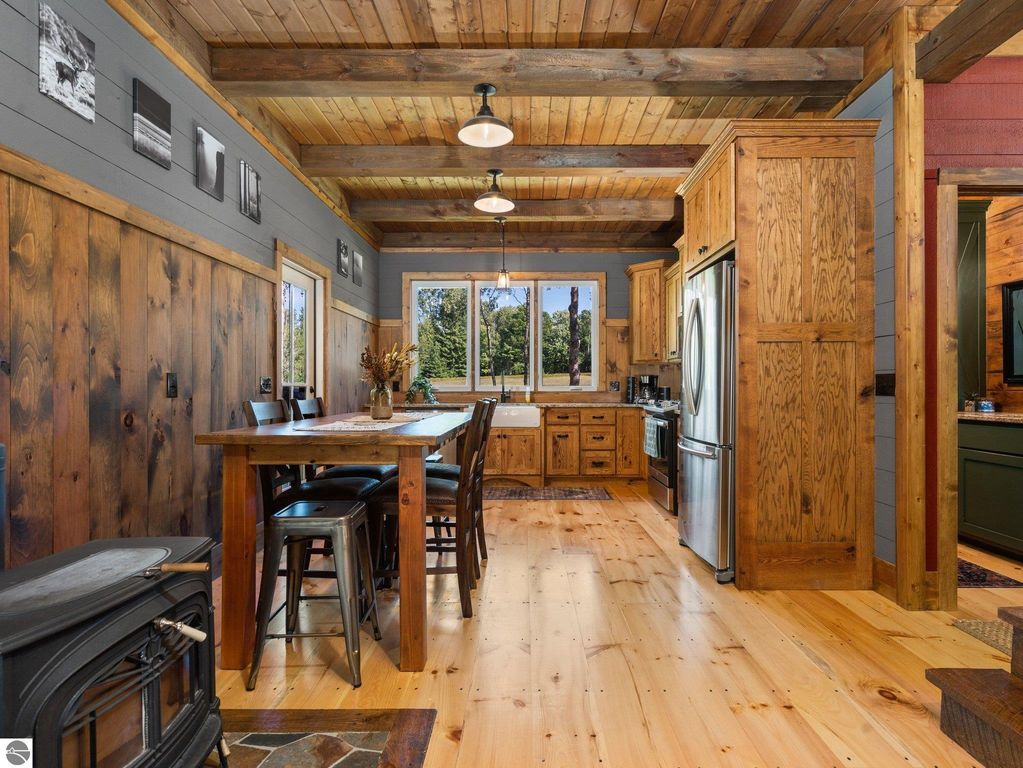 Custom-built kitchen and dining area with wooden cabinetry, large windows offering natural light, and rustic decor, showcasing the craftsmanship of the 4-bedroom home on 10 acres in Lake City, MI.