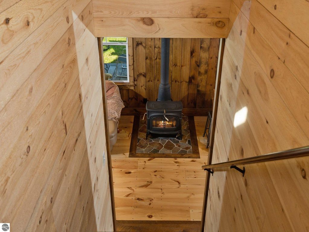Cozy interior view of custom-built home featuring a woodstove, natural wood walls, and large window overlooking the northern Michigan countryside, highlighting craftsmanship and warmth.