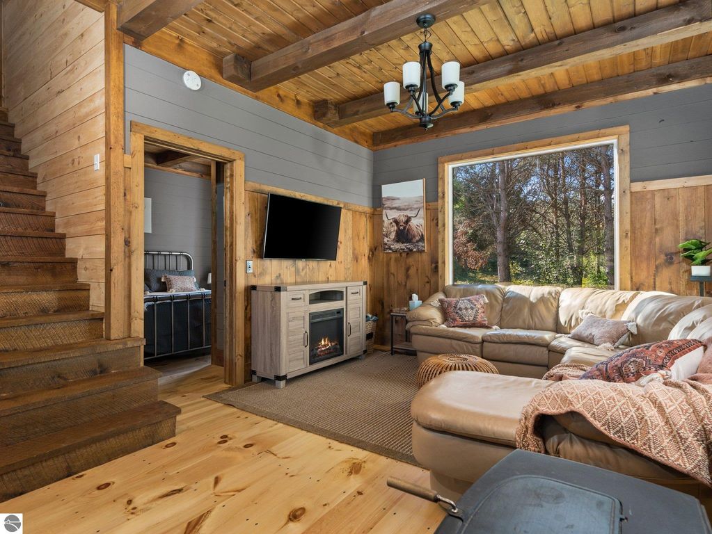 Cozy living room with custom wood finishes, large windows offering natural light, and a comfortable sectional sofa, showcasing the craftsmanship of the 4-bedroom, 2-bath home in Lake City, MI.