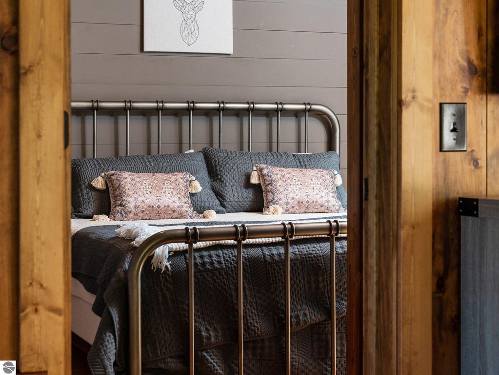 Cozy bedroom featuring a metal bed frame with decorative pillows and textured bedding, showcasing rustic wood accents and a serene atmosphere, reflecting the custom craftsmanship of the Lake City, MI home.