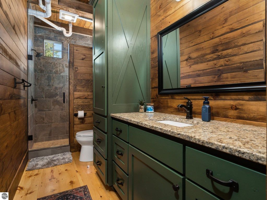 Custom bathroom featuring green cabinetry, granite countertop, and a walk-in shower with natural stone tiles, showcasing rustic wood accents and modern fixtures in a northern Michigan home.