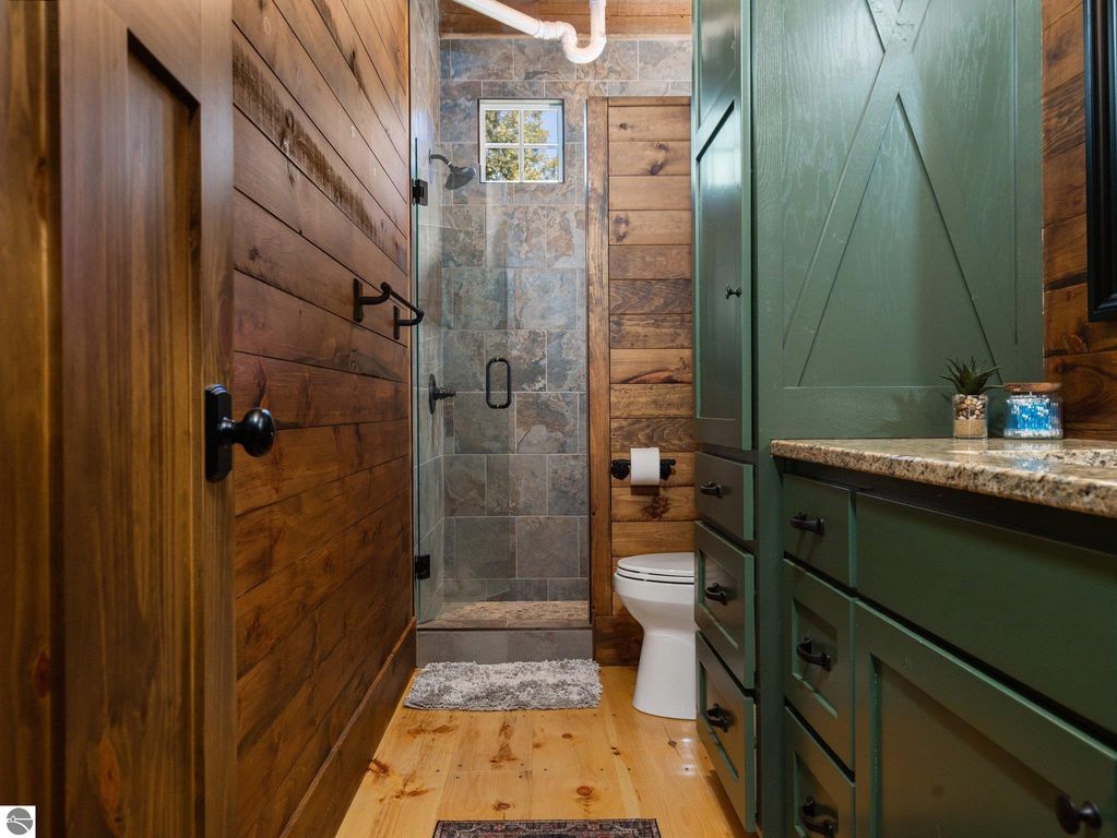 Custom bathroom interior featuring wood and stone accents, glass shower enclosure, green cabinetry, and natural light from window.