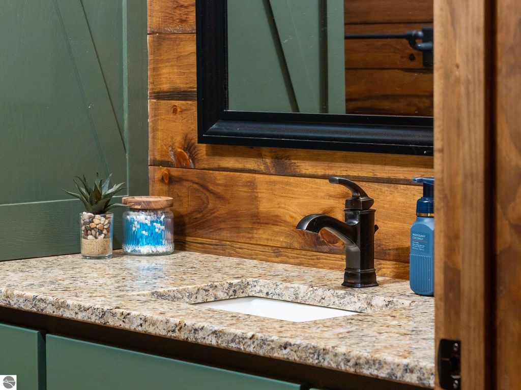 Custom bathroom sink with granite countertop, dark faucet, decorative plants, and storage jars, showcasing rustic charm in a northern Michigan home.