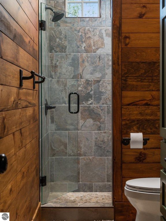 Custom shower with glass enclosure, stone tile walls, wooden accents, and modern fixtures in a northern Michigan home bathroom.