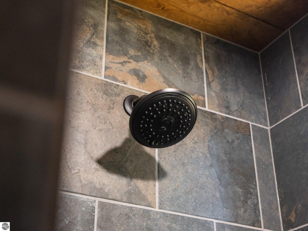 Showerhead in a custom bathroom featuring slate tile, showcasing modern design and craftsmanship in the 4-bedroom home at 5800 W Moorestown Road, Lake City, MI.