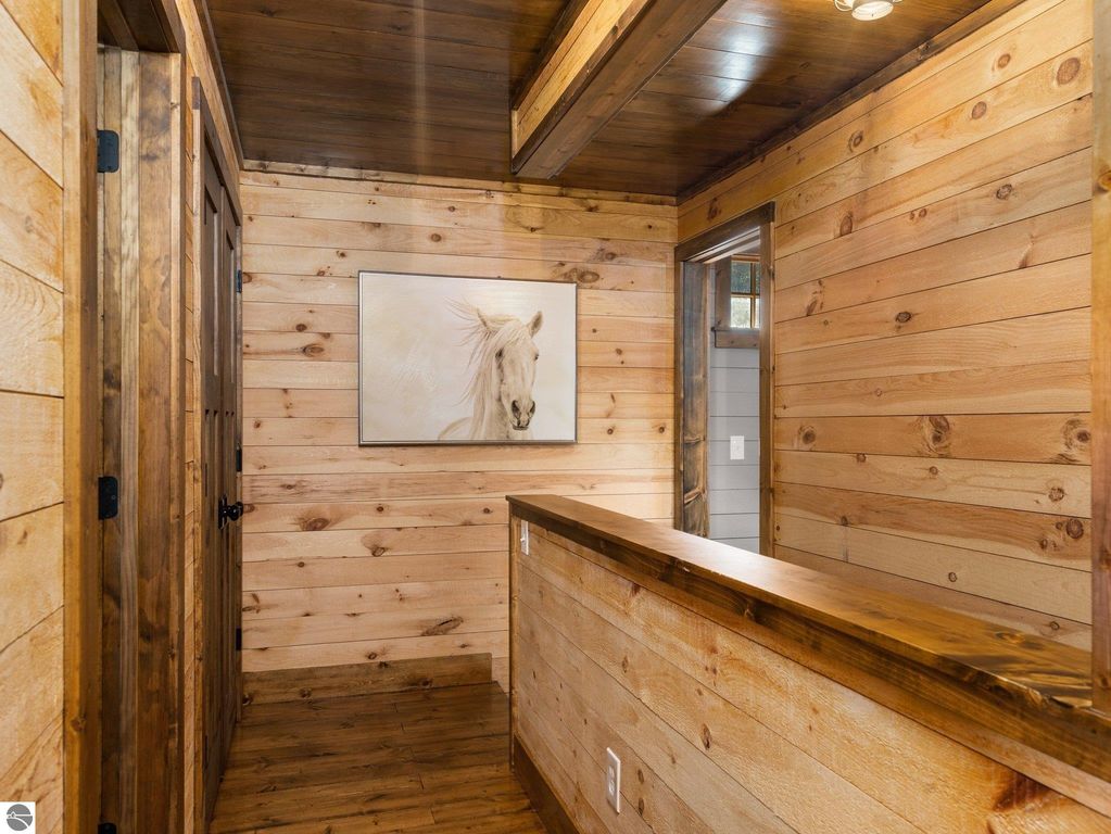 Custom wood interior hallway featuring a horse painting, handcrafted wooden doors, and rustic rough-sawn walls, reflecting the craftsmanship of the 4-bedroom, 2-bath home in Lake City, MI.