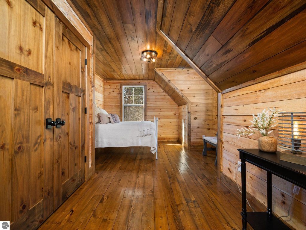 Cozy bedroom with rustic wood paneling, handcrafted furniture, and natural light highlighting the custom craftsmanship, located in a 4-bedroom home on 10 acres in Lake City, MI.