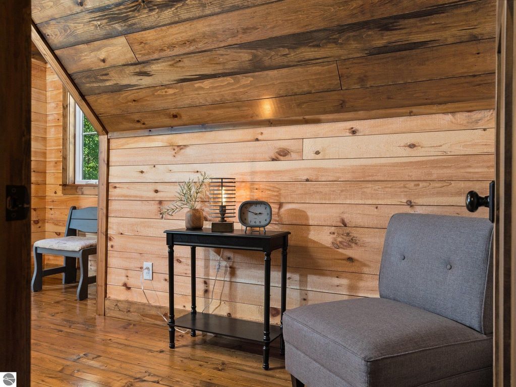 Cozy reading nook with a gray armchair, wooden side table, and decorative lamp against a backdrop of natural wood paneling in a custom-built home.