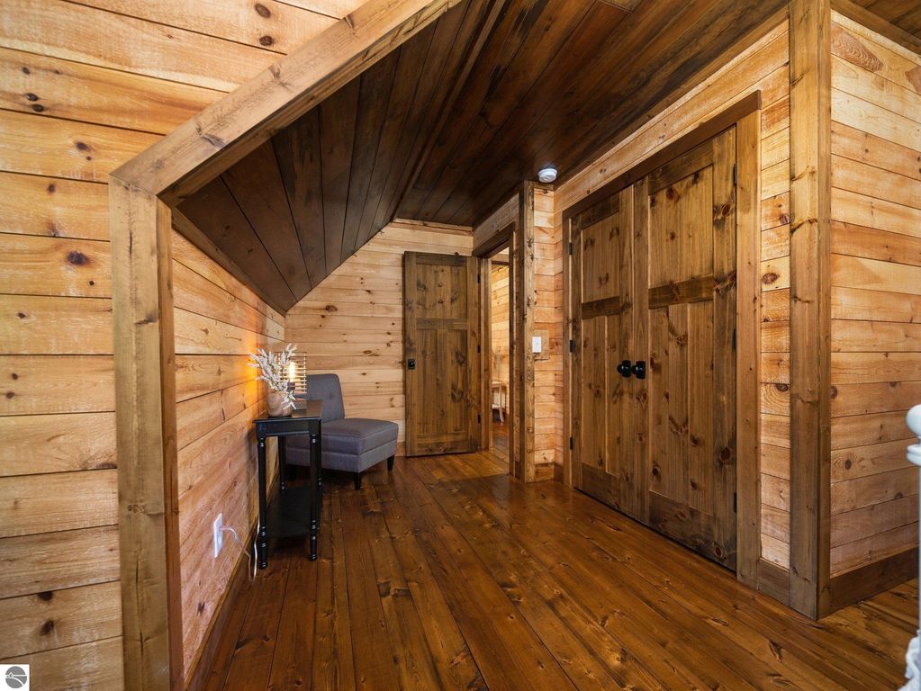 Wooden hallway with custom craftsmanship, featuring handmade doors, rough-sawn wood walls, and a cozy chair beside a small table, emphasizing the rustic charm of the 4-bedroom, 2-bath home in Lake City, MI.