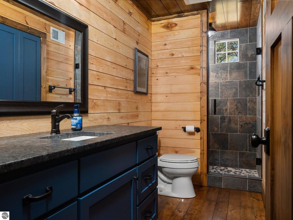 Bathroom featuring custom craftsmanship with wooden walls, dark cabinetry, modern fixtures, and a tiled shower, showcasing a blend of rustic and contemporary design elements.