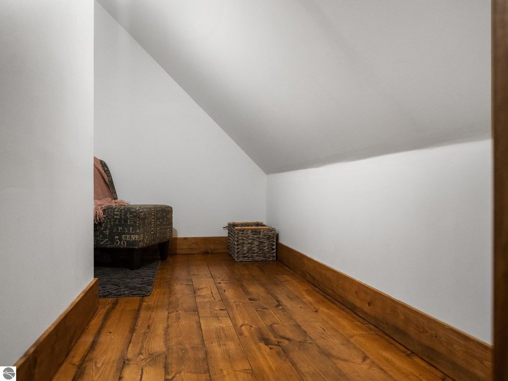 Cozy reading nook with a patterned chair and a wicker basket, featuring warm wooden flooring and sloped ceiling in a custom-built home in northern Michigan.