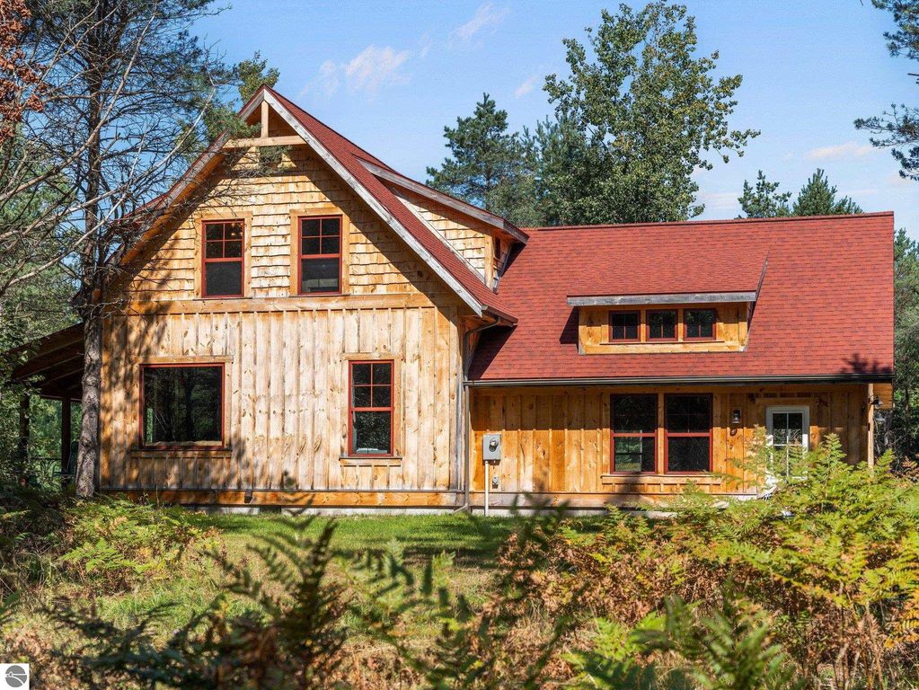 Custom-built wooden home with red accents surrounded by northern Michigan greenery, showcasing craftsmanship and serene countryside setting near Lake City.