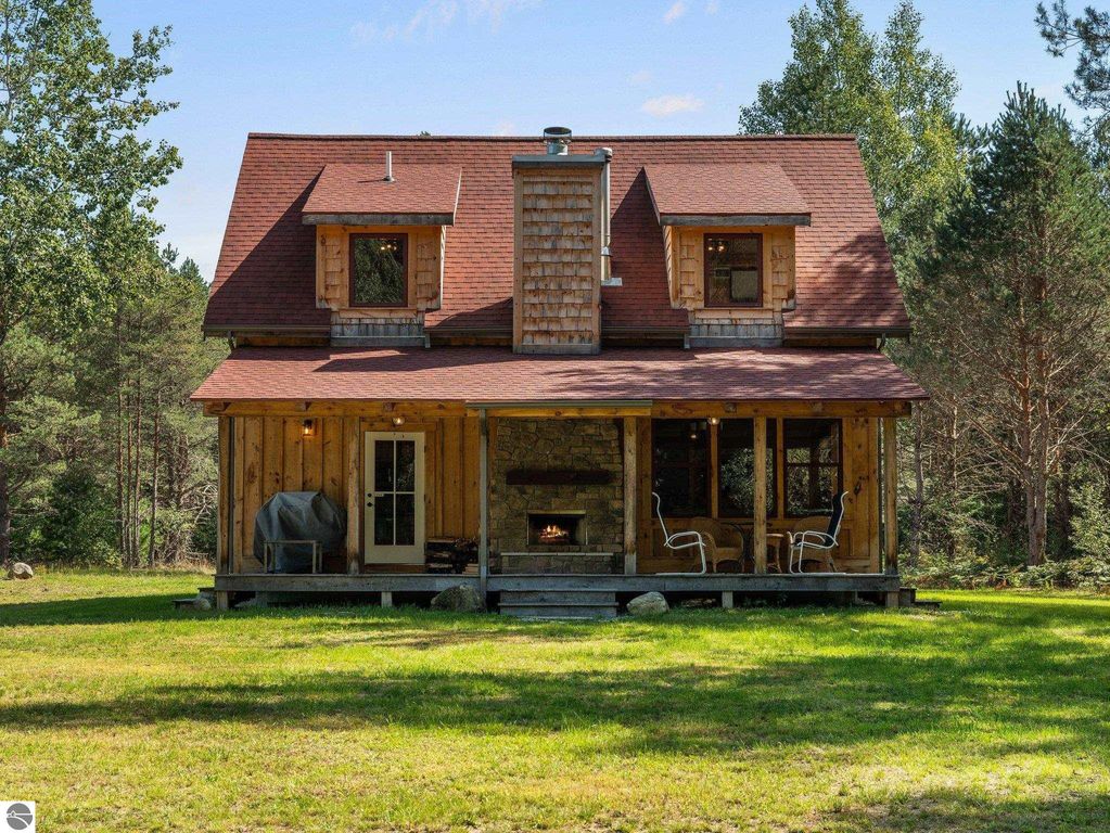 Custom-built 4-bedroom home in northern Michigan, featuring a rustic wooden exterior, covered porch, and stone fireplace, surrounded by lush greenery on 10 acres of countryside.