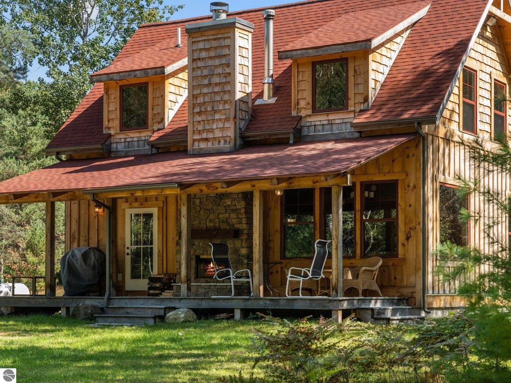 Custom-built home with wooden exterior, red roof, stone fireplace, and covered porch, surrounded by greenery on 10 acres in Lake City, MI.