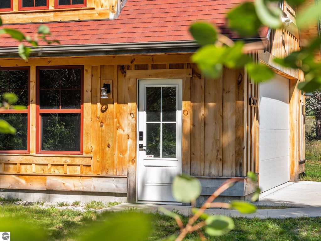 Custom-built home exterior featuring natural wood siding and red trim, showcasing large windows and a welcoming front door, set on a picturesque 10-acre property in Lake City, MI.