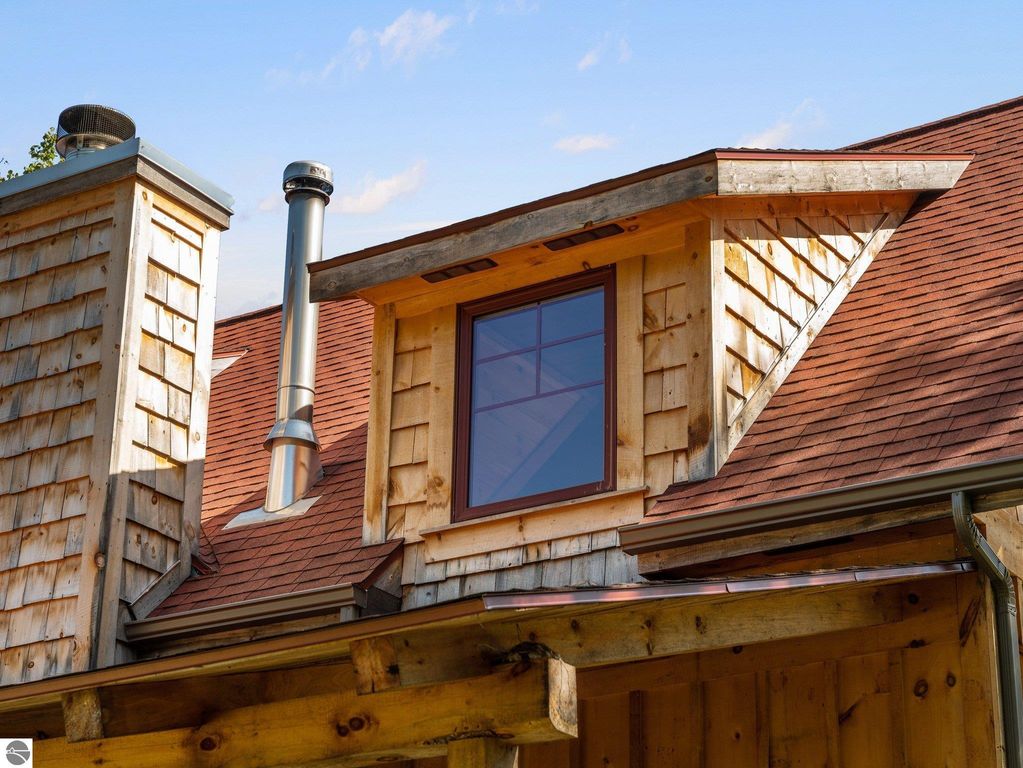 Custom-built home exterior featuring wooden shingles, a red roof, and a large window in the gable, showcasing northern Michigan craftsmanship.