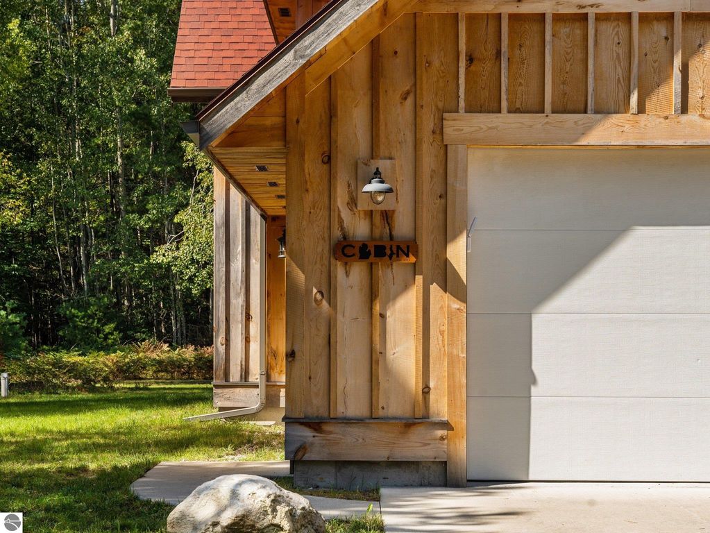 Custom-built cabin exterior with wooden siding, stone feature, and "Cabin" sign, surrounded by northern Michigan greenery, reflecting serene countryside living.