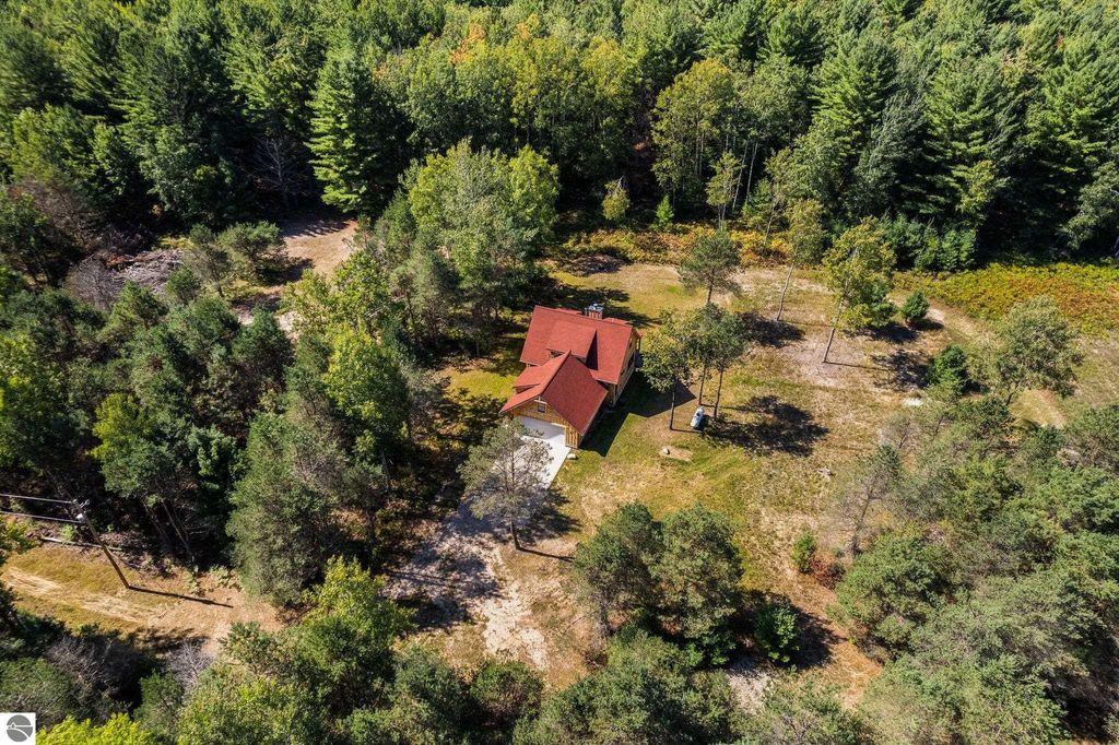 Aerial view of a custom-built home with a red roof surrounded by lush greenery on 10 acres in Lake City, MI, showcasing northern Michigan countryside and natural beauty.