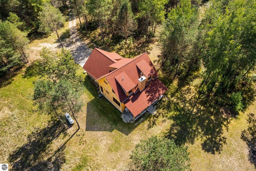 Aerial view of a custom-built 4-bedroom, 2-bath home on 10 acres in Lake City, MI, surrounded by trees and featuring a red roof, showcasing the serene northern Michigan countryside.