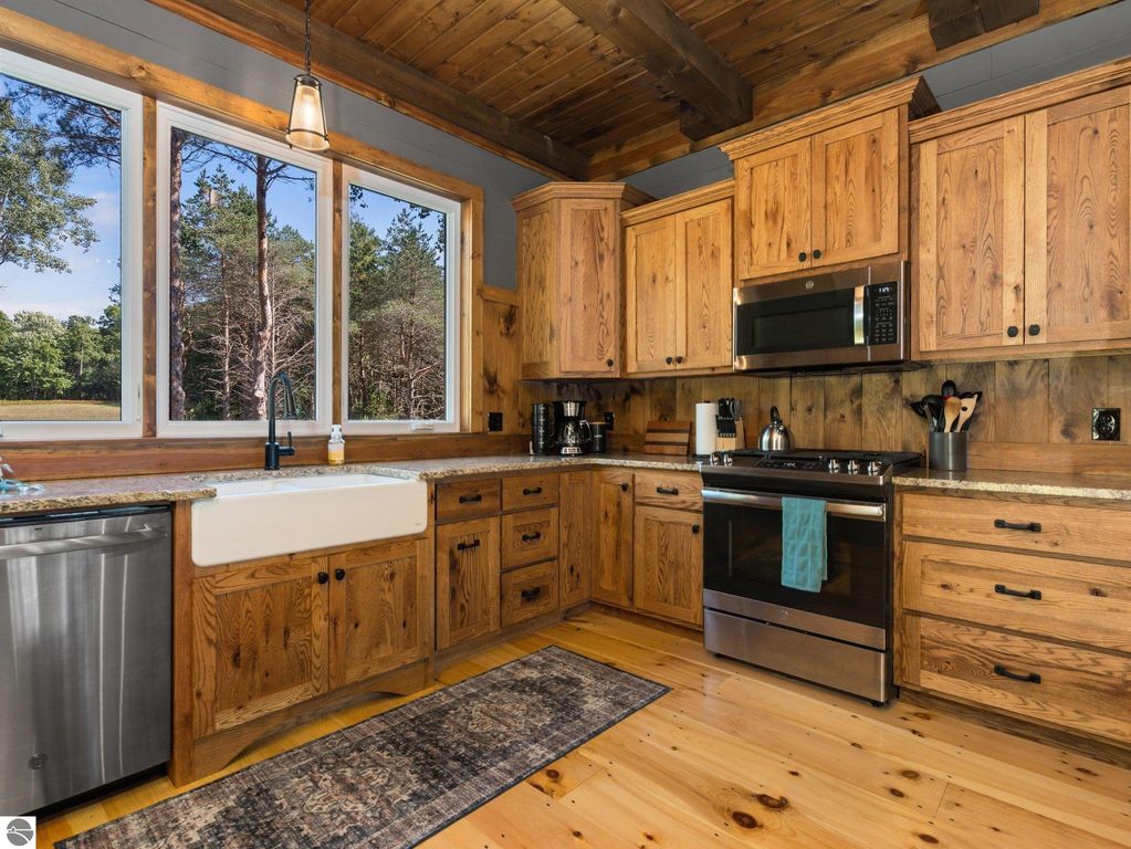 Custom kitchen with rustic wooden cabinets, stainless steel appliances, large windows showcasing northern Michigan nature, and a farmhouse sink, highlighting craftsmanship and open-concept design in a 4-bedroom home.
