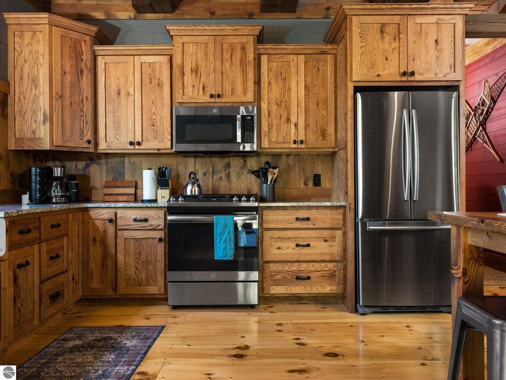 Custom kitchen with rustic oak cabinets, stainless steel appliances, and granite countertops, showcasing a warm and inviting design in a 4-bedroom home on 10 acres in Lake City, MI.