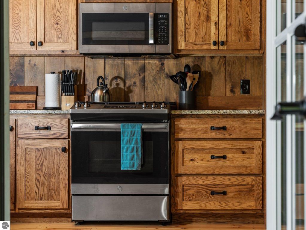 Custom kitchen featuring oak cabinetry, stainless steel appliances, granite countertops, and a teal towel hanging from the stove, showcasing the warm, rustic design of the home at 5800 W Moorestown Road, Lake City, MI.