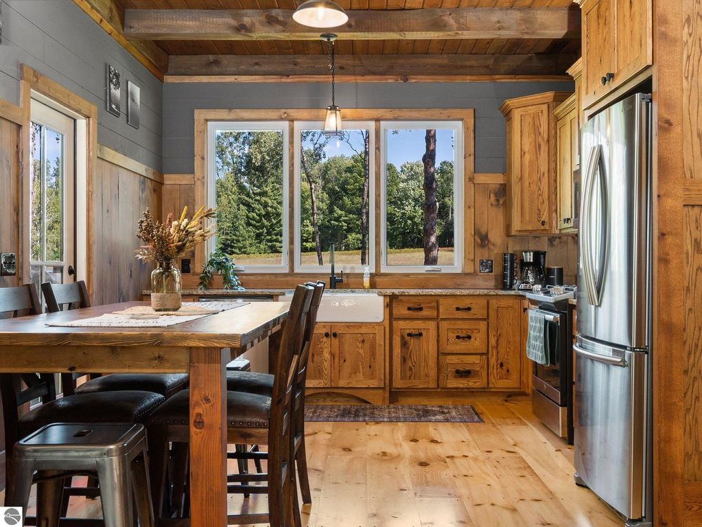 Custom-built kitchen with rustic wood cabinetry, large windows showcasing northern Michigan countryside, dining table, and modern appliances.