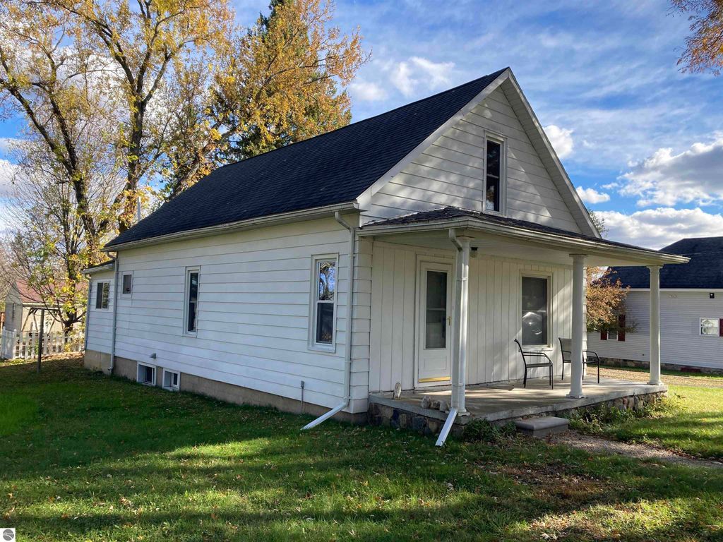 Cozy three-bedroom home exterior at 206 George Smith Jr. Street, Rose City, MI, featuring a covered front porch, large yard, and surrounding trees.