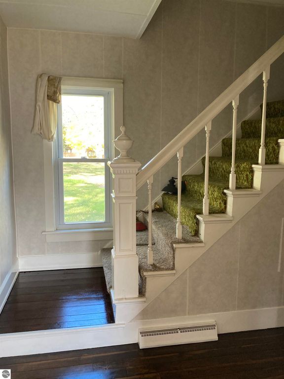 Interior view of a staircase with white railing and green carpet, showcasing a window with natural light in a cozy home at 206 George Smith Jr. Street, Rose City, MI.