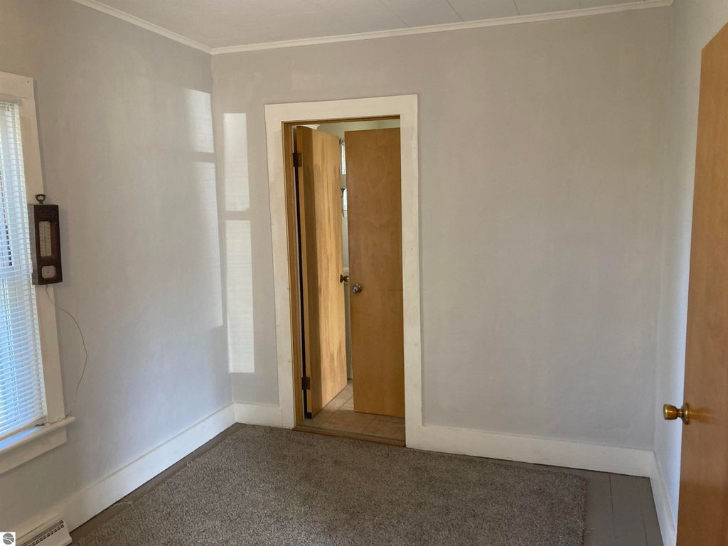 Interior view of a cozy room in a home for sale at 206 George Smith Jr. Street, featuring light gray walls, carpeted flooring, a window with blinds, and an open doorway leading to another room.