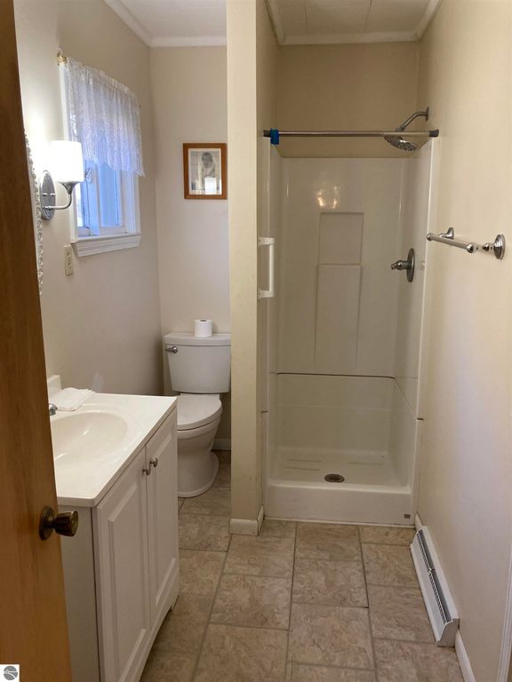 Bathroom with shower, toilet, and white vanity in cozy home at 206 George Smith Jr. Street, Rose City, MI.