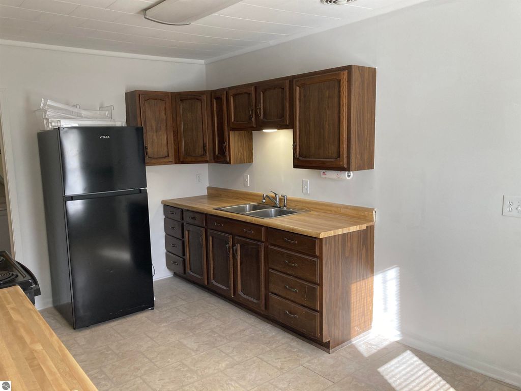 Kitchen interior featuring wooden cabinets, black refrigerator, and sink, highlighting spacious layout in Rose City home listing.
