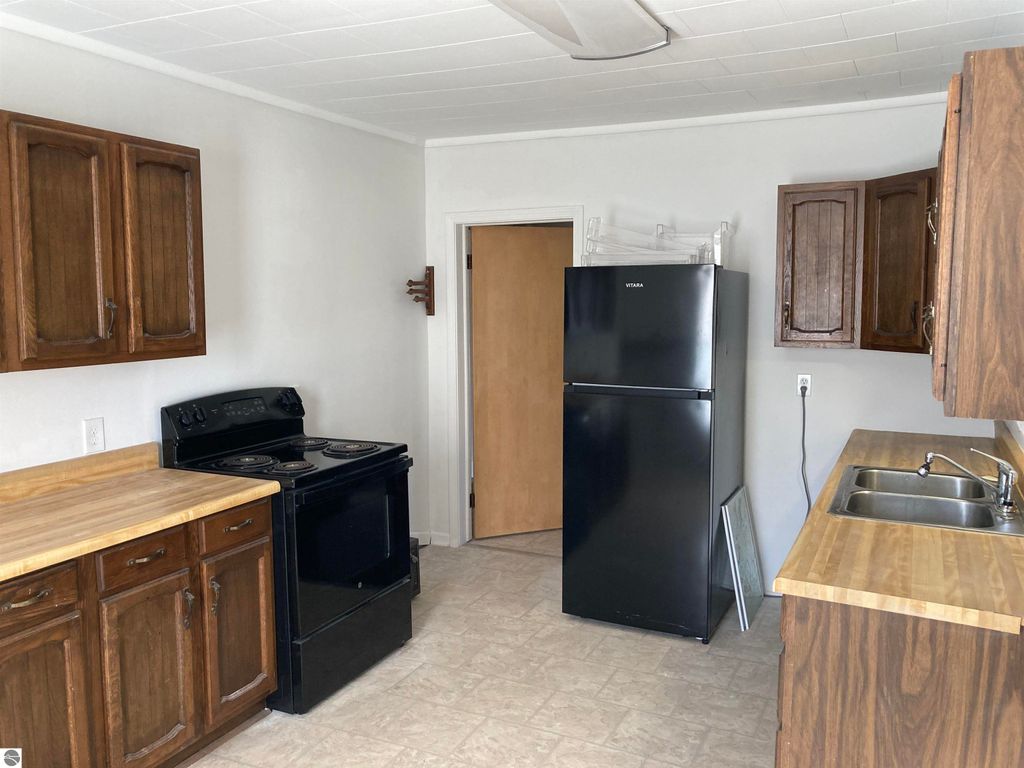 Kitchen interior of a cozy home in Rose City, featuring wooden cabinets, a black stove, a black refrigerator, and a double sink, highlighting the functional layout and move-in ready condition.