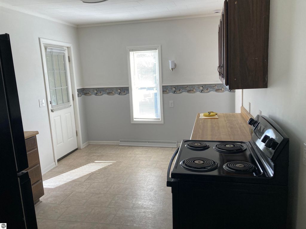 Kitchen interior of a cozy home in Rose City, featuring a black stove, wooden countertop, and natural light from a window, with a door leading outside and a decorative border along the wall.
