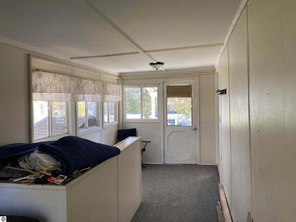 Enclosed back porch of a cozy home in Rose City, featuring large windows, a door leading outside, and a cluttered surface with a blue blanket, emphasizing the property's inviting atmosphere.