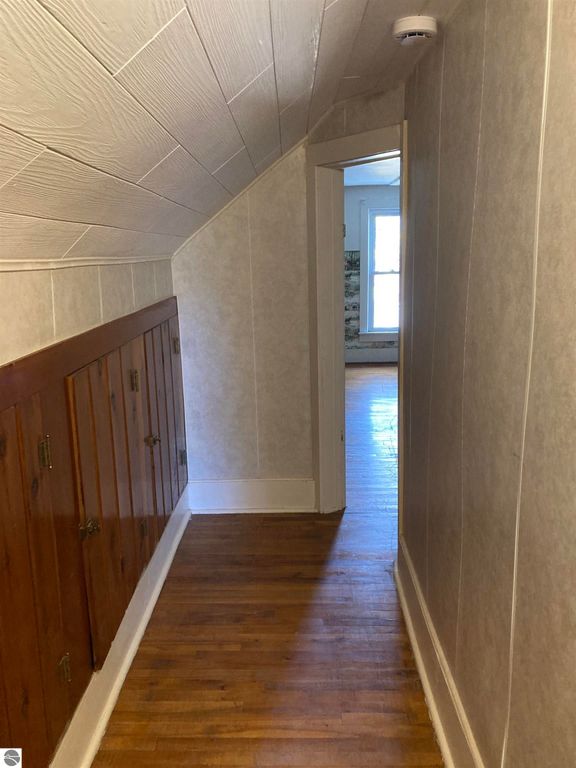 Hallway with wood paneling, leading to an open doorway, showcasing natural light and hardwood floors in a cozy Rose City home.