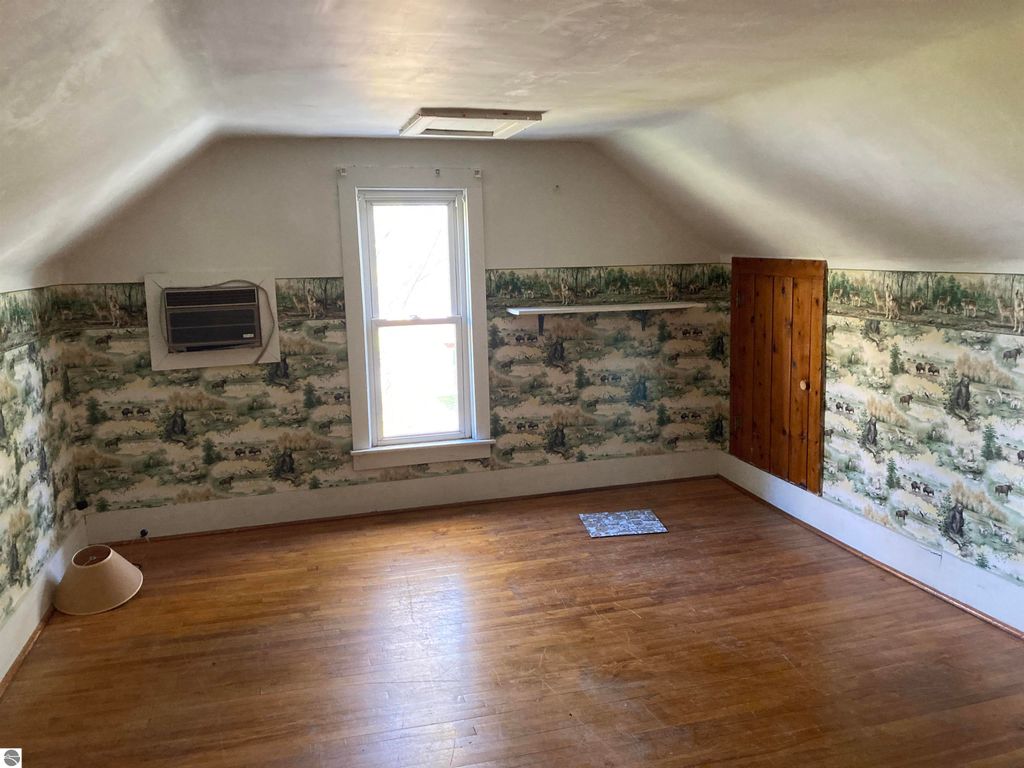 Cozy bedroom in Rose City home featuring wood floors, air conditioning unit, and decorative wallpaper with nature scenes.
