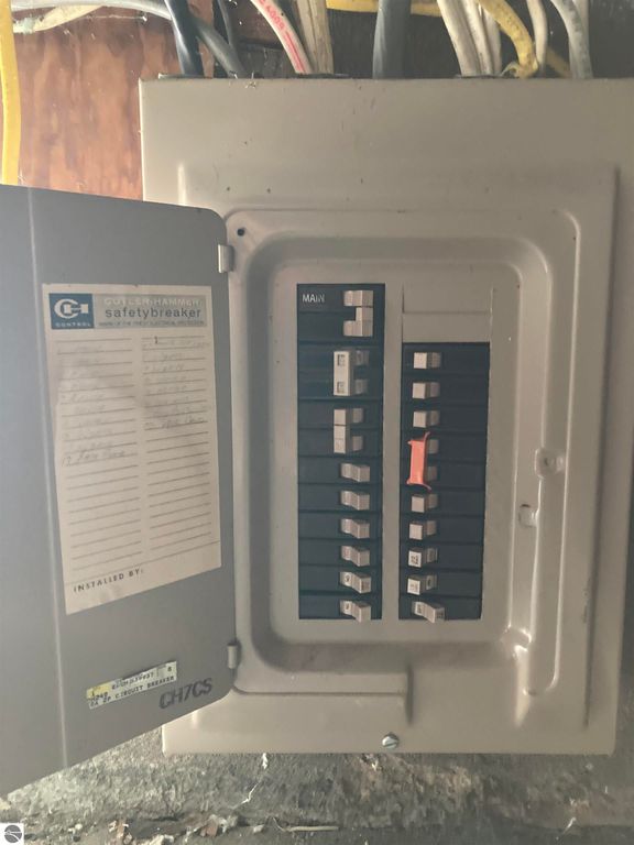 Electrical panel with circuit breakers, including a main switch and labeled switches, located in the basement of a home in Rose City, MI.