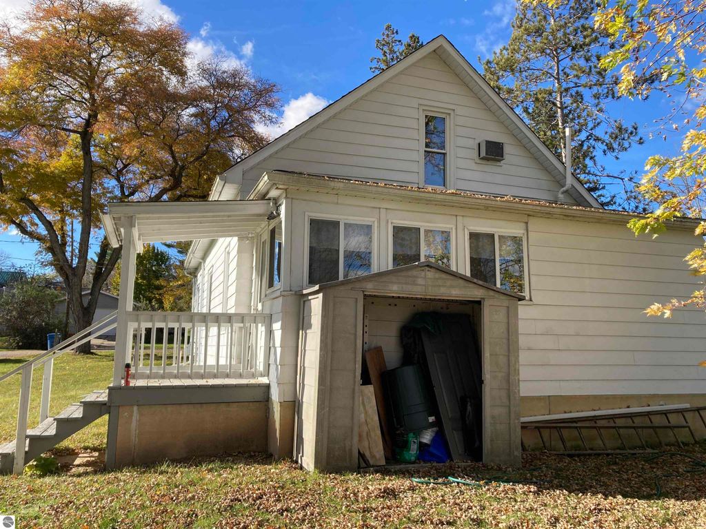 Cozy single-family home exterior at 206 George Smith Jr. Street, Rose City, MI, featuring a covered front porch, enclosed back porch, and storage shed, surrounded by autumn foliage.