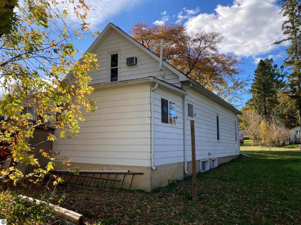 Side view of a cozy single-family home in Rose City, MI, featuring a white exterior, large windows, and surrounded by autumn foliage, highlighting its quiet location and spacious yard.