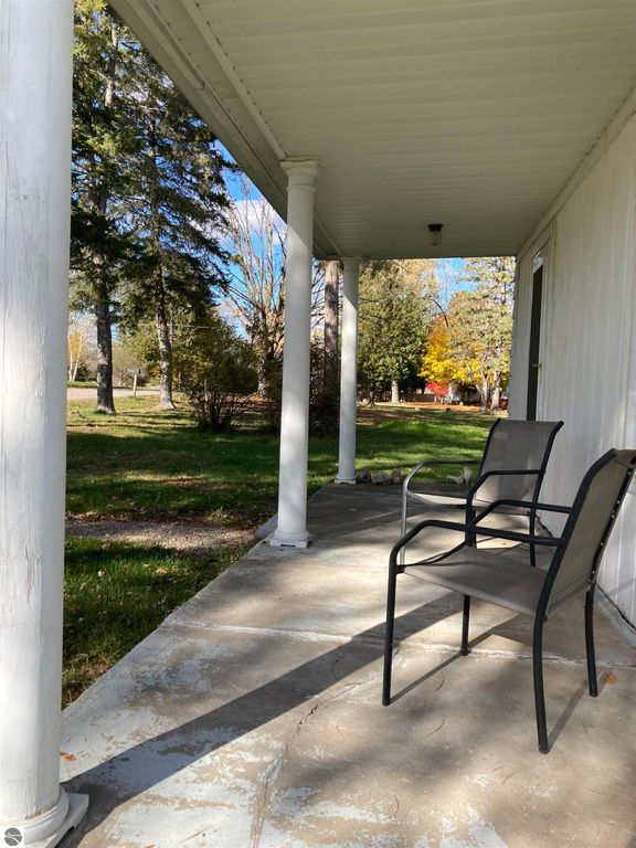 Front porch view of 206 George Smith Jr. Street, Rose City, MI, featuring two chairs, white columns, and a landscaped yard with trees.