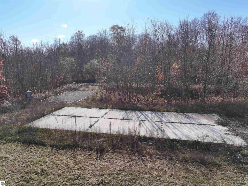 Wooded 8-acre parcel in Buckley, MI, featuring a cleared concrete pad for building, surrounded by trees and nature, with electrical service and RV hookup on site.