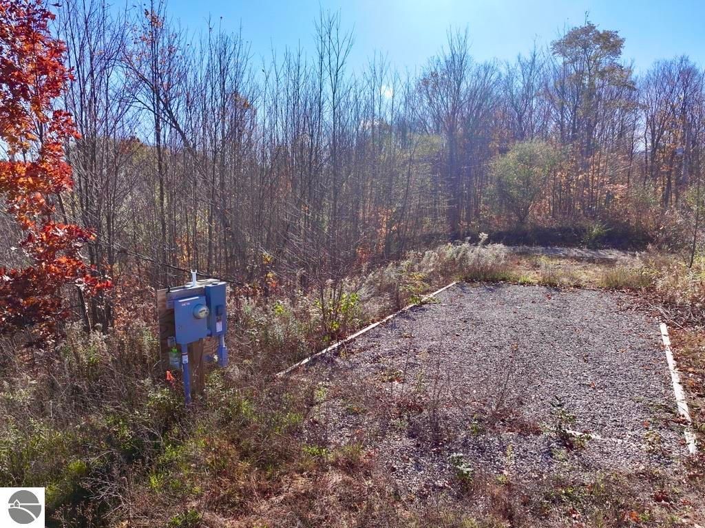Cleared gravel pad for building with electrical service in wooded area, showcasing 8-acre parcel at 6884 Zue Road, Buckley, MI.
