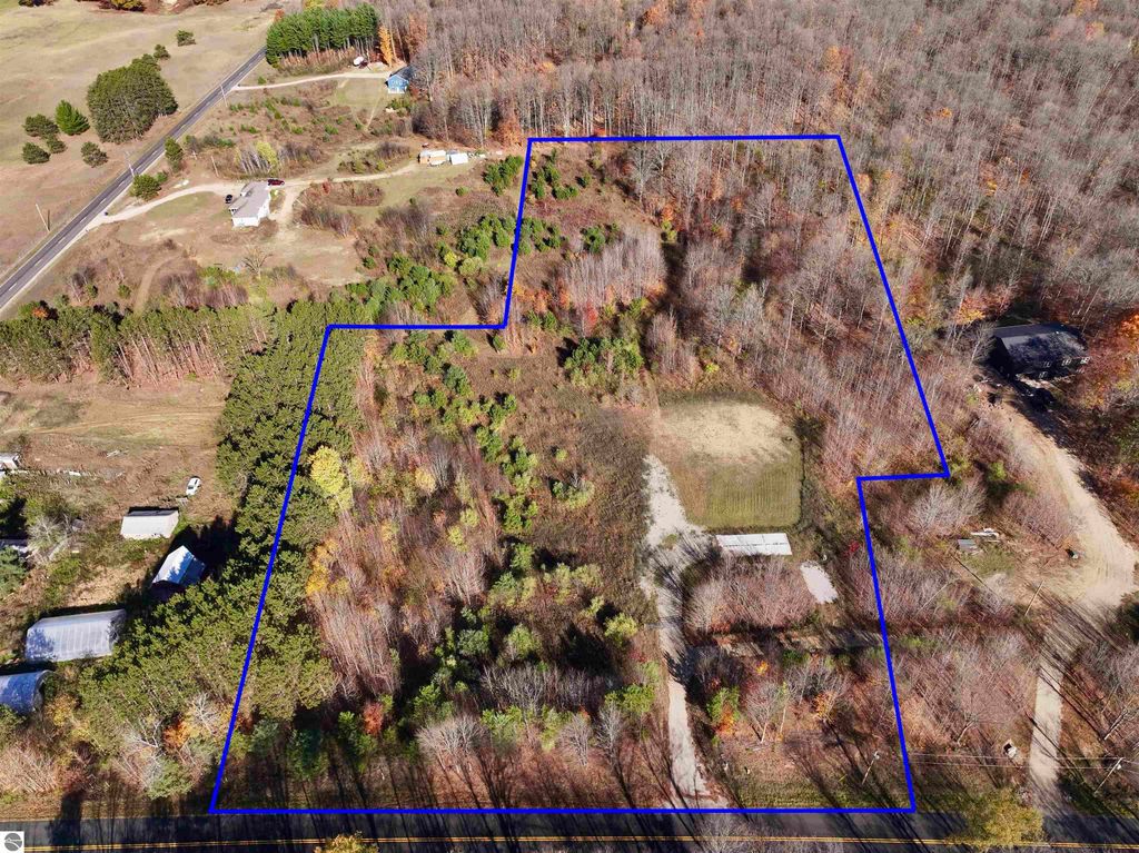 Aerial view of an 8-acre wooded parcel at 6884 Zue Road, Buckley, MI, featuring a cleared area for building, surrounded by nature, with established trails and nearby recreational access.