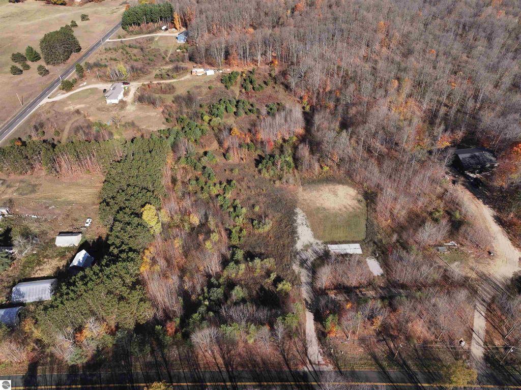 Aerial view of 8-acre wooded parcel at 6884 Zue Road, Buckley, MI, featuring cleared area for building, surrounding trees, and nearby roads, ideal for privacy and nature enthusiasts.