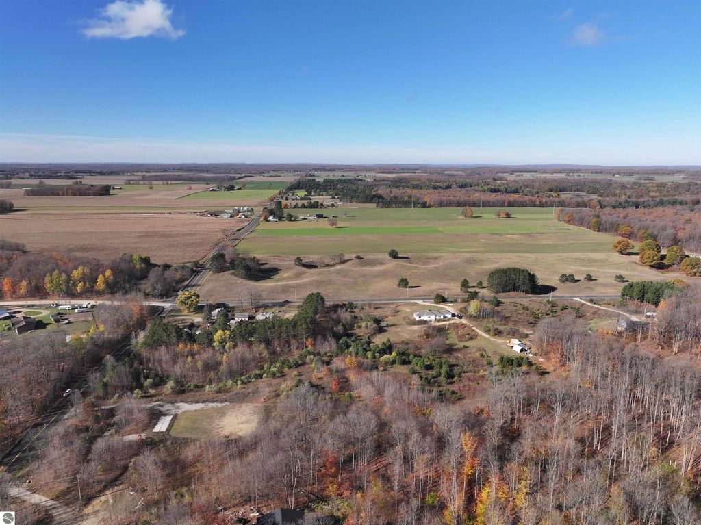 Aerial view of 6884 Zue Road, Buckley, MI, showcasing 8-acre wooded parcel with nearby recreational trails and open fields, ideal for building a home or enjoying nature.