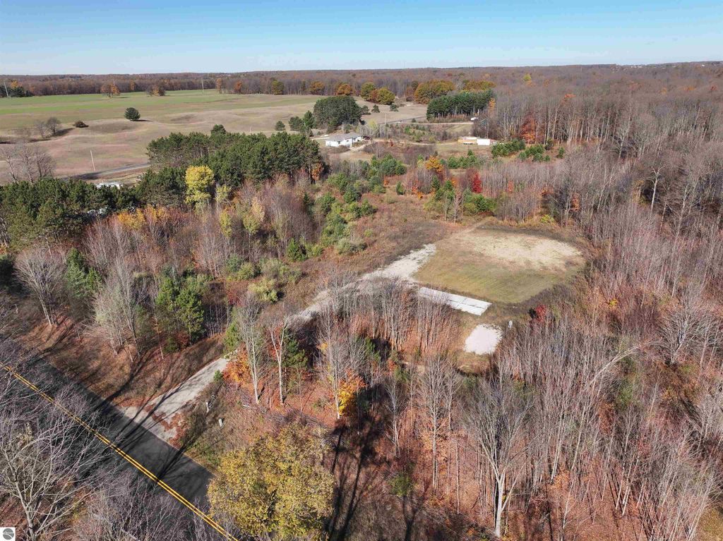 Aerial view of an 8-acre wooded parcel at 6884 Zue Road, Buckley, MI, showcasing a cleared area for building, surrounded by trees and open fields, highlighting the property’s natural beauty and potential for recreational use or residential development.